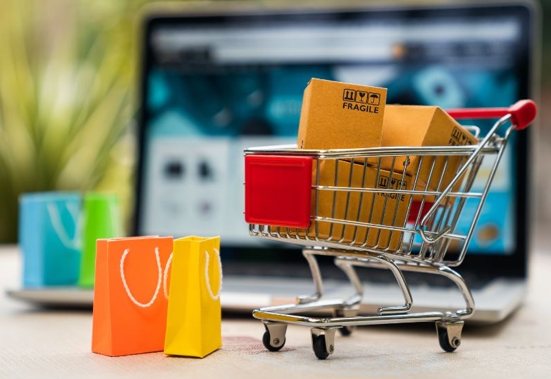 Einkaufswagen mit bunten Shoppingtaschen mit einem Laptop im Hintergrund